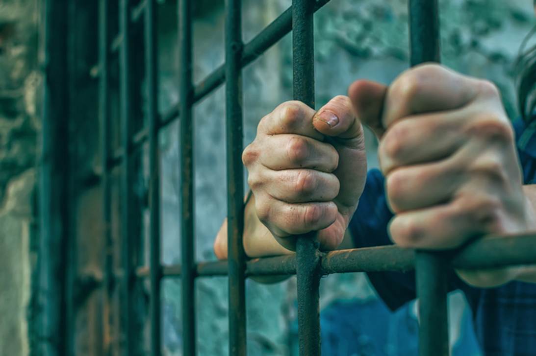 Close up on clenched fists gripping jail bars. The image illustrates an article on false imprisonment by law enforcement.